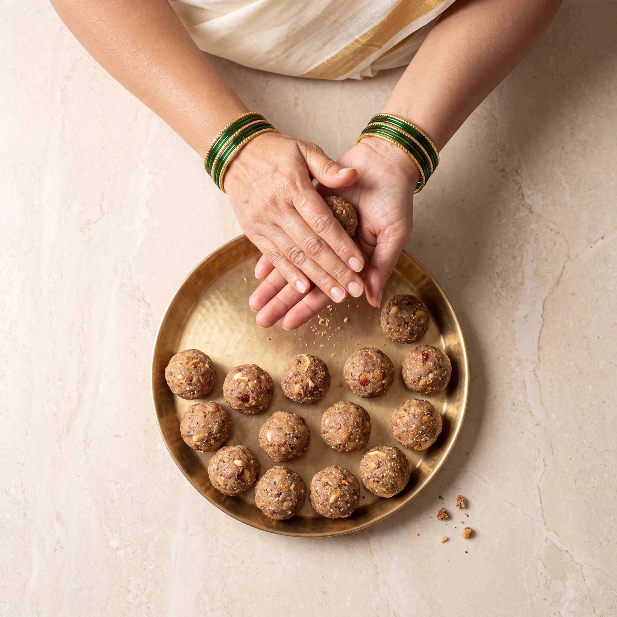 Hands shaping a laddoo above a tray of finished laddoos